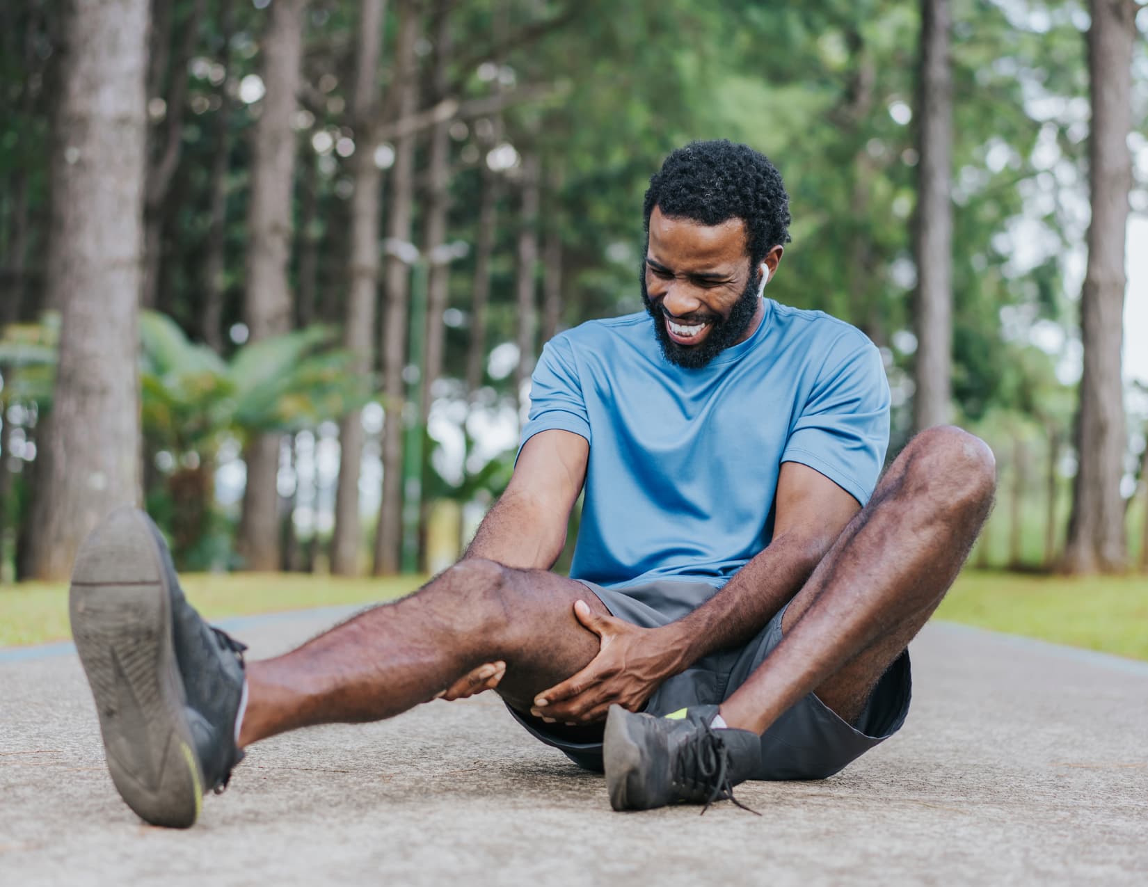 Runner sits in the center of a trail, gripping his knee and grimacing in pain.